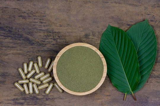 Mitragyna Speciosa Korth or kratom powder on wooden bowl wtih capsules and green leaf on rustic wooden background, top view and copy space.