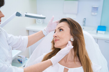 Doctor examining a woman face with both gloved hands