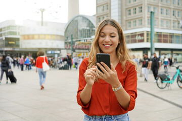 Portrait of smiling young woman using a mobile app in Berlin city street, Germany