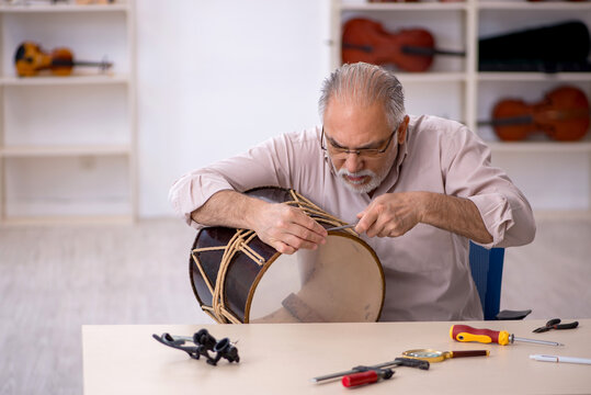 Old male repairman repairing musical instruments at workshop