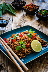 Asian food - soba noodles, stir fried vegetables, soy sauce and mushrooms on wooden table
