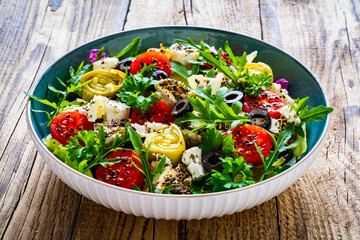 Fresh salad - feta cheese, artichokes, cherry tomatoes, black olives and greens on wooden table
