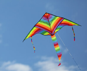 colorful triangular kite that flies high in the sky with some clouds tied to a thread