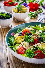 Fresh salad - feta cheese, artichokes, cherry tomatoes, black olives and greens on wooden table
