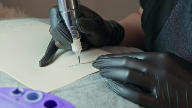 Eyebrow tattoo. hands in black protective gloves with a machine for permanent makeup do a test coloring of the eyebrows on a silicone mat. permanent makeup master training