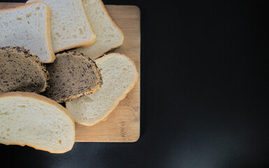 Various types of bread baked and cut on a wooden board on a black background. With space for text