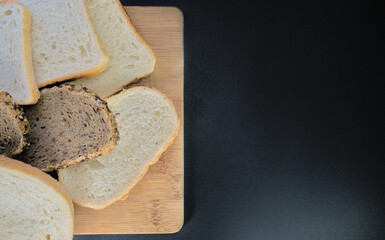 Various types of bread baked and cut on a wooden board on a black background. With space for text