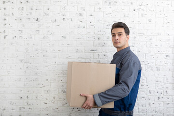 Confident male contractor from moving service holding box beside white brick wall background