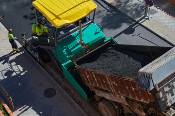 Aerial view of a paver, road paving machine, with a load of new asphalt that will be used to renovate a street. Bitumen and tar used to renew the pavement at roadwork with an asphalt finisher vehicle.