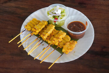 top view ten sticks of pork satay with dipping sauce, placed on a banana leaf on a paper plate, on wooden background, food, copy space