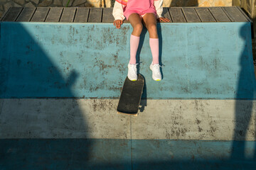 Female child in bright clothes sitting at the rollerdrome with her skateboard
