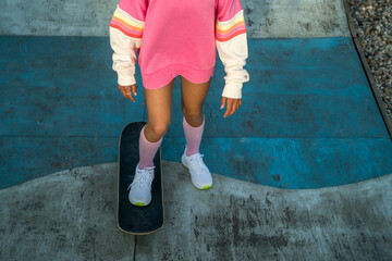 Fototapeta na wymiar Little girl in bright clothes riding at the skateboard at the rollerdrome while enjoying