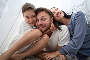Cheerful hugs of dad, mom and son in cozy, fabulous hut