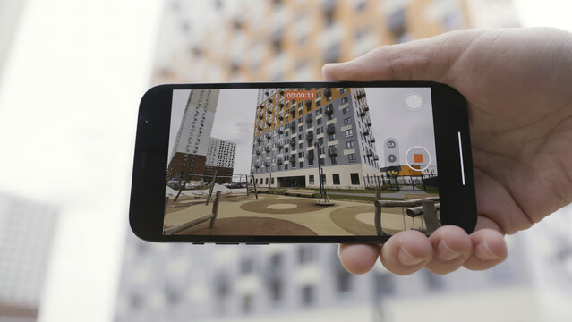 Close up of male hands recording a video on a smartphone in wide angle mode. Action. Amazing quality of a picture, shooting a multi storey building on a new device.