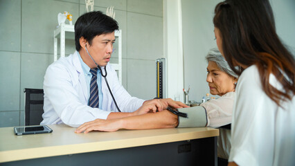 Fototapeta premium Male doctor measures the blood pressure of a senior female patient in the examination room.
