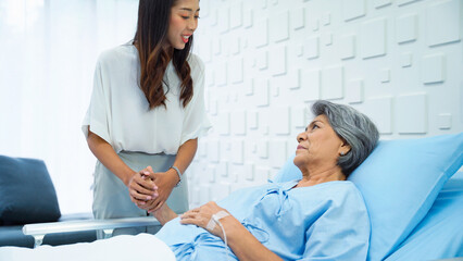 Fototapeta premium Young woman holding hands to support Sick mother, receiving saline, in bed in the hospital room. Young woman gently massages her arm to her mother who is resting.