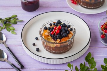 Cottage cheese casserole or soufflé with blueberry jam, fresh blueberries and red currants in portion molds on a purple wooden background.