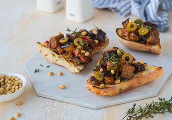 Sicilian caponata, eggplant, tomato and olive stew on white bread on a marble board against a light concrete background. Vegetable appetizer.