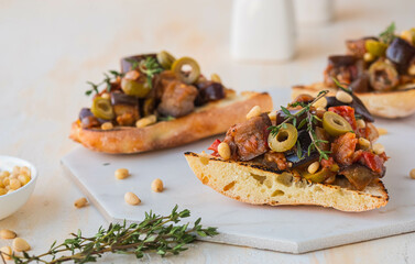 Sicilian caponata, eggplant, tomato and olive stew on white bread on a marble board against a light concrete background. Vegetable appetizer.