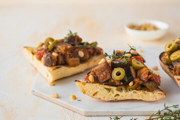 Sicilian caponata, eggplant, tomato and olive stew on white bread on a marble board against a light concrete background. Vegetable appetizer.