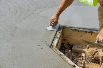 An employee of construction company uses a stainless steel edger to form corner in the new cement...