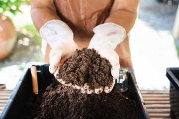 Farmer shows hands holding fertile soil and earthworms on blur background.