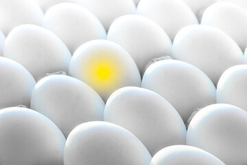 Yellow light in one egg among many white eggs.Creative concept photography.The concept of the idea and the origin of life