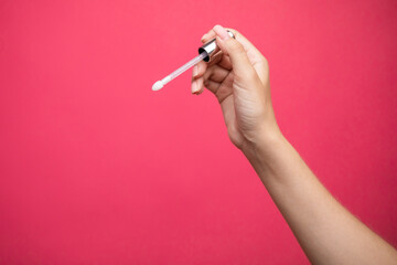 Hands holding lip gloss applicator on pink background.