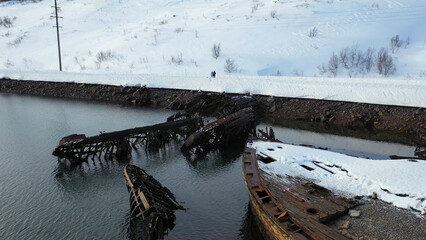 Aerial view of cemetery of old rusty ships near the snowy coast of cold sea in winter season....