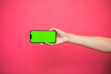 Woman hand Holding a Green Screen Smartphone on pink background.