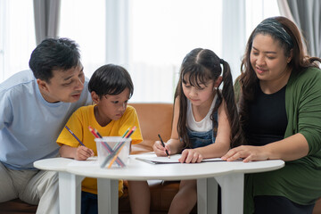 Asian parents teaching and helping kids to do homework at home, family spending time together. mother and father taking care of son and daughter. support knowledge and education