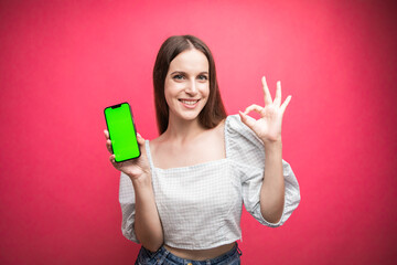 Happy woman standing and hold smartphone and gesting okay on pink background. Green screen phone screen