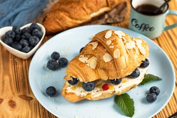 Croissant sandwich with cheese , arugula and berries. classic american breakfast. Fresh french croissant with fresh berries. blueberry and strawberry on cream cheese. Croissant and a cup with coffee 