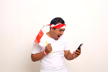 Happy Indonesian man standing while holding cellphone and indonesian flag. Independence day concept