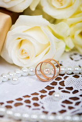 two gold wedding rings and bouquet of white rose with green leaves on a wooden
