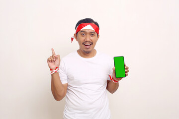 Naklejka premium Asian man standing while showing blank cellphone screen and pointing side. Independence day concept