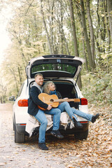 Romantic couple sitting in a trunk of white car in a forest with a guitar