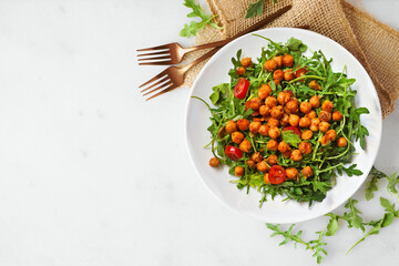 Salad of arugula and seasoned chickpeas. Top view on a white plate over a white marble background with copy space.