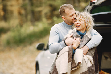 Romantic couple standing in a forest near their white car