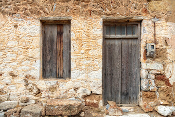 Old rural home facade. Weathered stonewall cottage exterior, wooden brown window and door. Greece