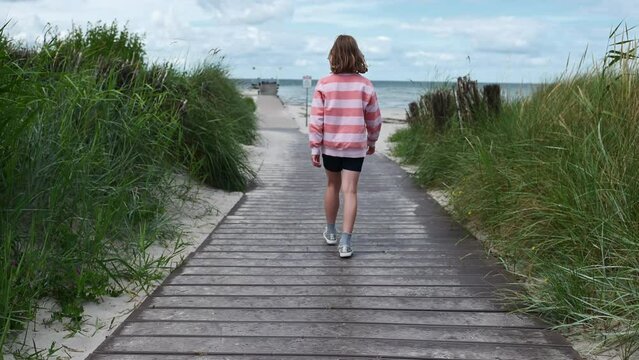 Teenage girl walking on pathway on white beach at windy weather at summer vacation