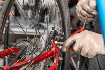 Master in protective gloves tightens the bolts on the bicycle system of a sports bike with a hex wrench. Professional repair and service of sports bikes