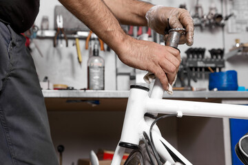 Close up of hand of a mechanic in protective gloves putting a bearing on a bicycle pipe in a workshop. Maintenance of bicycle components and parts by a professional mechanic in the service workshop
