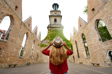 Tourism in Germany. Young woman tourist visiting the ruins of the church of Aegidienkirche destroyed during the bombing of the World War II in Hanover, Germany. - obrazy, fototapety, plakaty