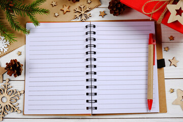A notebook with blank sheets and a pen, fir branches, wooden figures on a Christmas background.The...