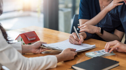Young married couple talking to a real estate agent to sign a house purchase contract.