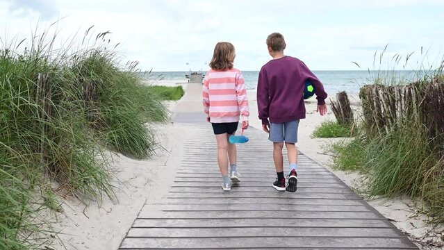 Slow motion 4K video of walking children on wooden pathway at white beach in north germany at summer vacation