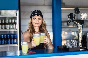 Hipster girl bartender serving fresh lemonade behind counter at outdoor bar during summer festival - 518994788