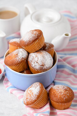 Homemade muffins with powdered sugar in a blue bowl and teapot on a striped napkin