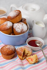 Homemade muffins with filling, teapot, cream and jam on a striped napkin